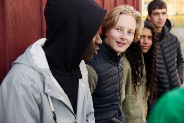 Fyra ungdomar står på rad, tre av dem tittar in i kameran.