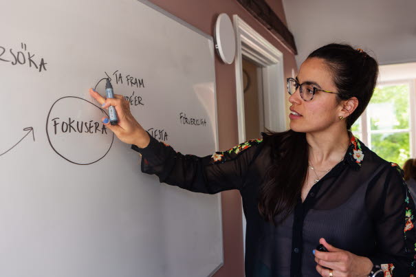 Person skriver text på whiteboard. Foto.
